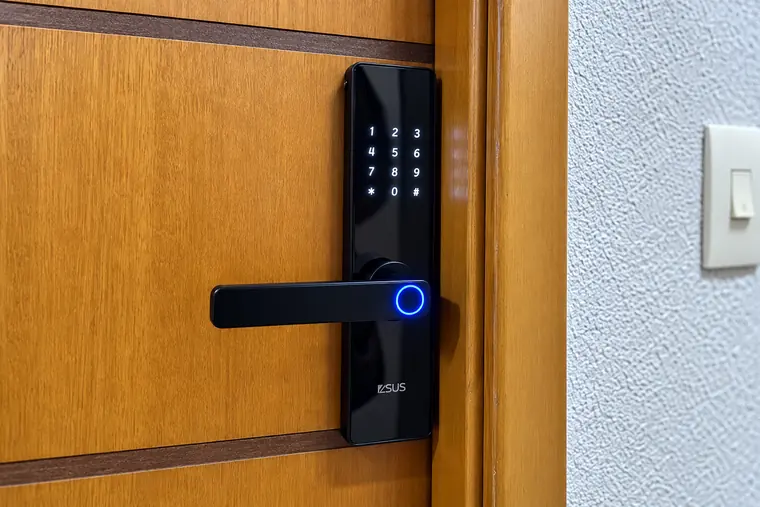 Fechadura digital ZSUS preta com leitor biométrico iluminado em azul e teclado numérico, instalada em porta de madeira